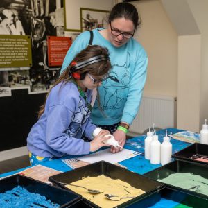 A child wearing ear defenders, with an adult, making a craft activity