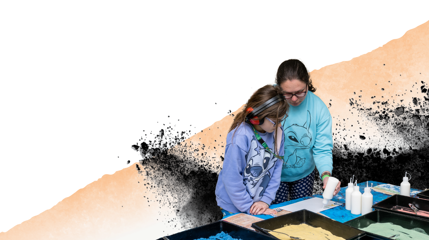 A mother and daughter doing crafts together. The child is wearing ear defenders and a sunflower lanyard.