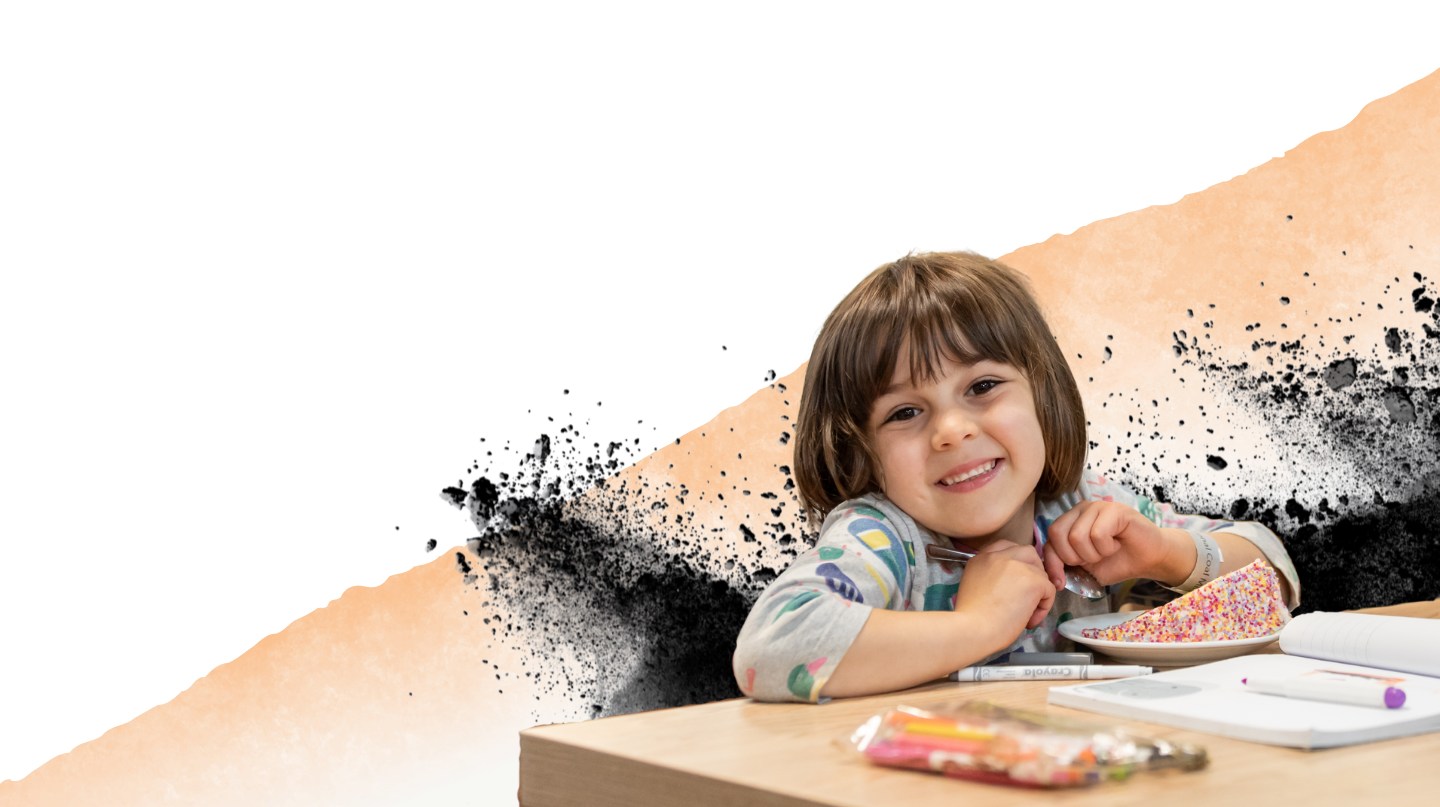 A child smiling with a large slice of colourful cake and a colouring book in front of her